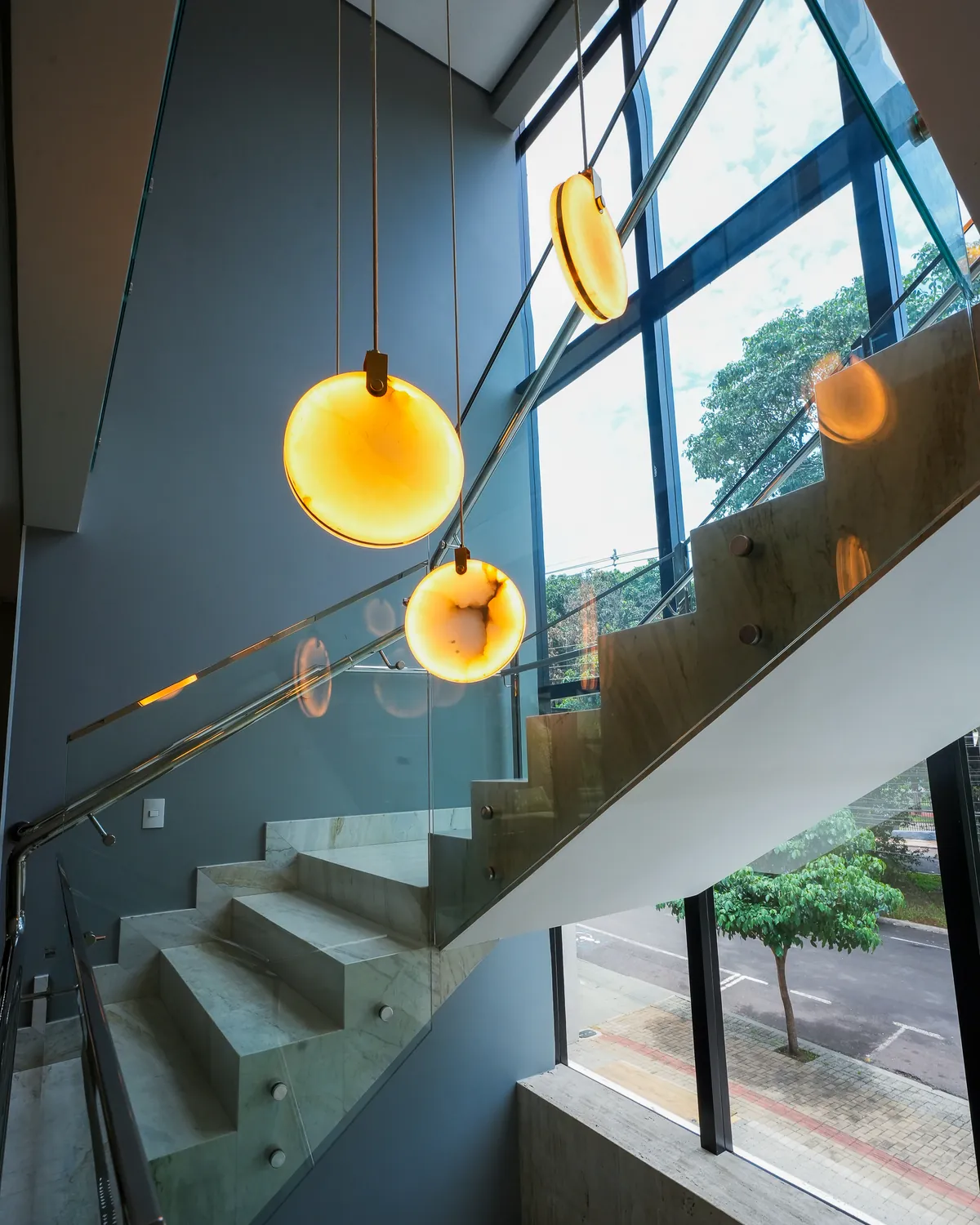 Escada com guarda-corpo de vidro e pendentes de luz na Pontello Corpo e Saúde